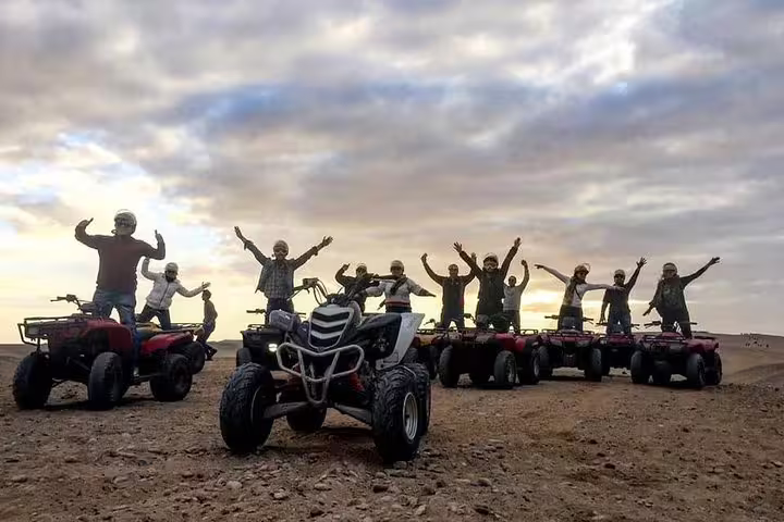 Group quad biking in Giza Desert at sunset, cheering on ATVs during pyramids safari adventure tour