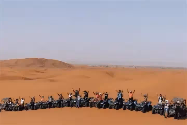 Group of enthusiastic riders on quad bikes lined up on vast sand dunes in Merzouga Erg Chebbi Desert.