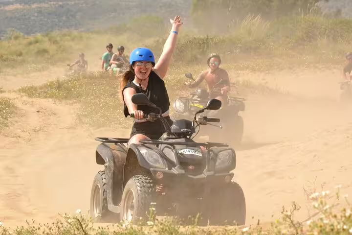 Excited rider raising an arm while leading a quad biking tour through dusty trails near Kusadasi Port.