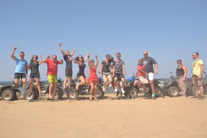 A group of excited tourists jumps in the air in front of their quads on a sunny beach near Kusadasi Port.