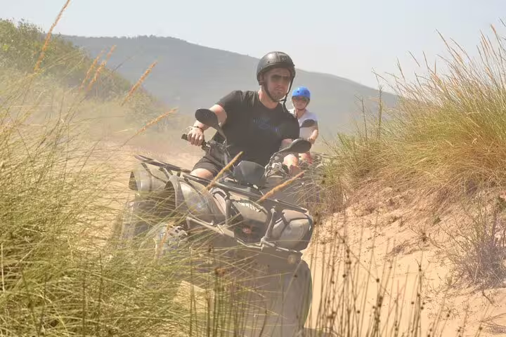 Two riders navigate sandy trails on quads, surrounded by greenery, near Kusadasi Port for an adventurous tour.