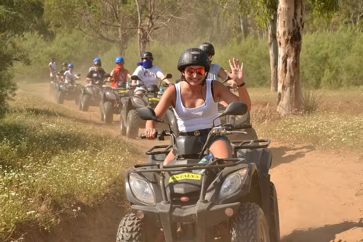 Cruise guests enjoy a thrilling quad ride through lush trails near Kusadasi Port, wearing helmets and smiling.