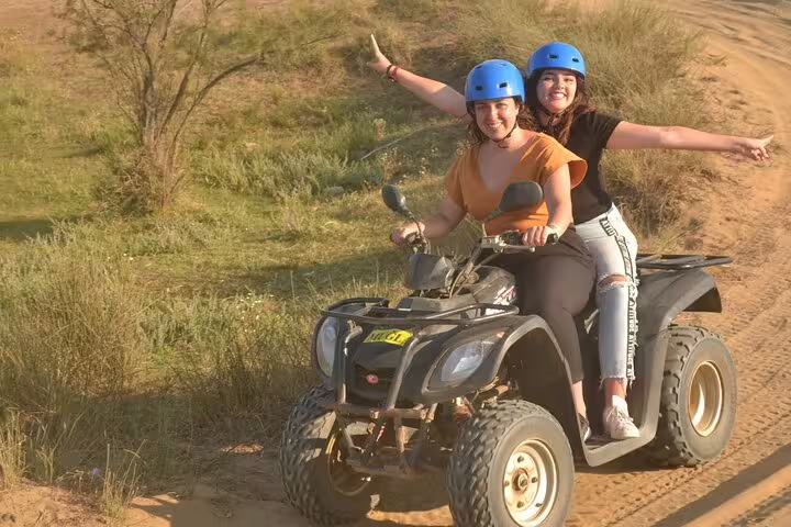 Two smiling women in blue helmets enjoy a thrilling quad ride on a dirt path near Kusadasi Port.