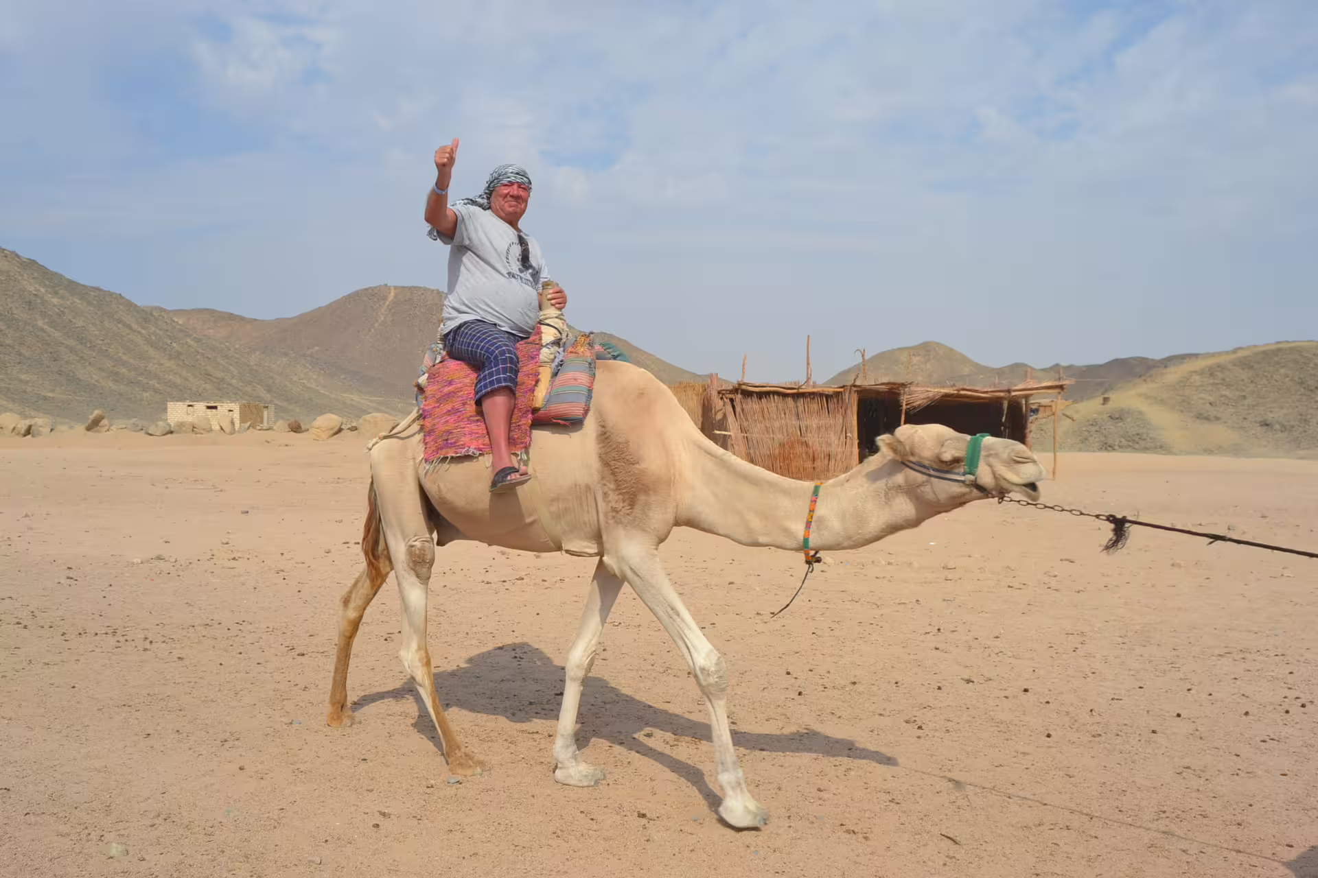 Camel ride stop on Hurghada quad tour, traveler crossing desert near Bedouin camp and rocky hills