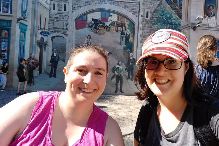 Happy travelers selfie by Old Quebec trompe-l’oeil mural on Quebec City scavenger hunt walking tour