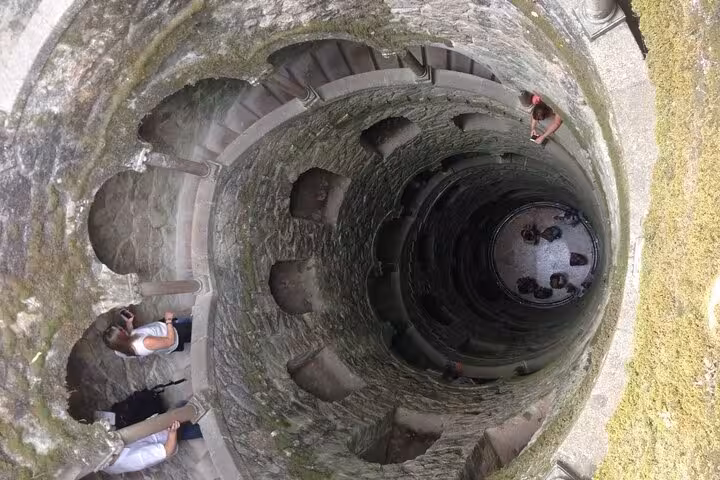 Tourists exploring the mystical Initiation Well at Quinta da Regaleira, showcasing its spiral staircase and unique architecture.