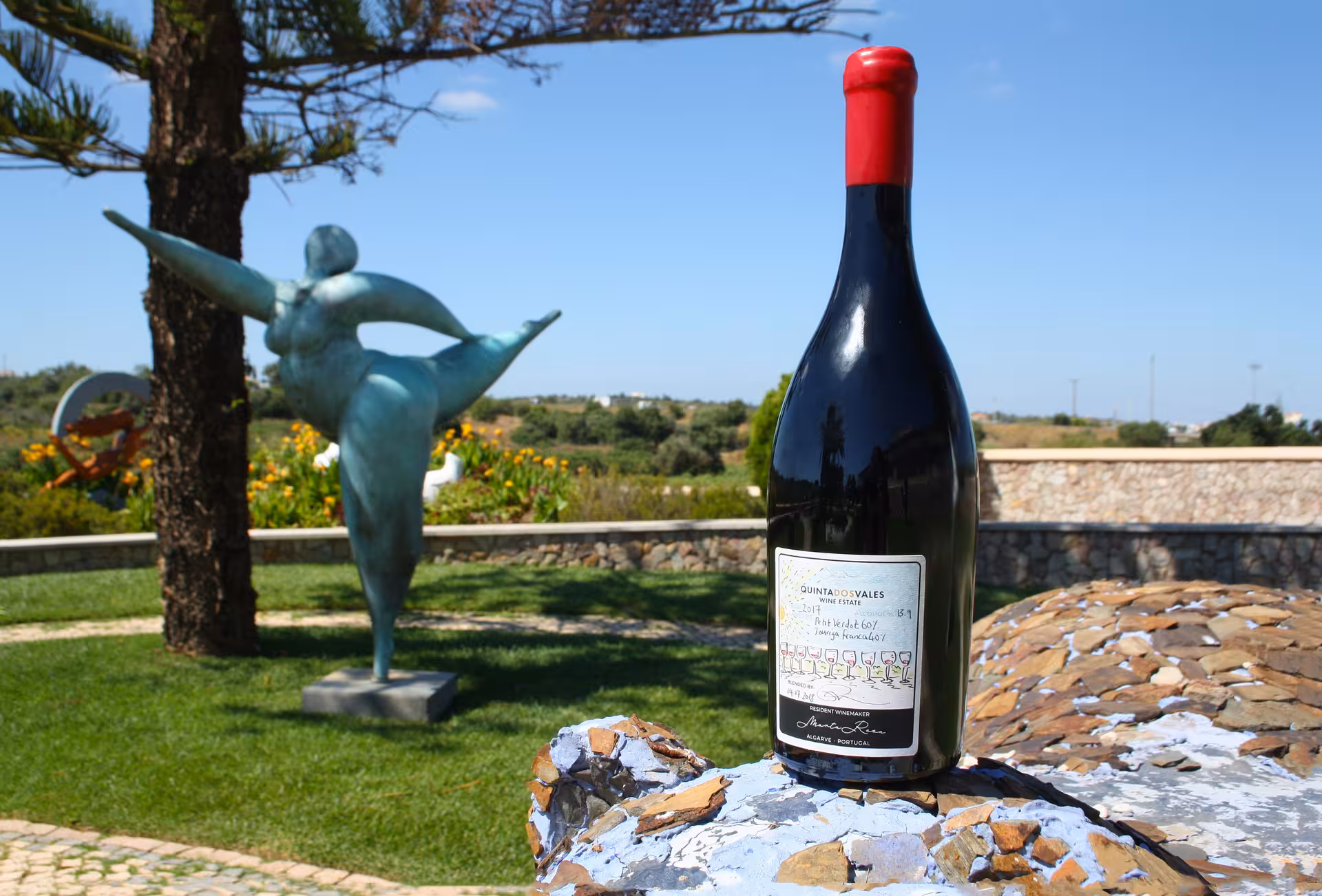 Quinta dos Vales wine bottle with red cap displayed on stone surface beside a bronze sculpture in Algarve Portugal during a bottle blending workshop