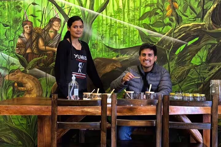 Couple enjoying cacao tasting at a rustic table in Quito, surrounded by vibrant rainforest-themed decor, during a hidden gems tour.