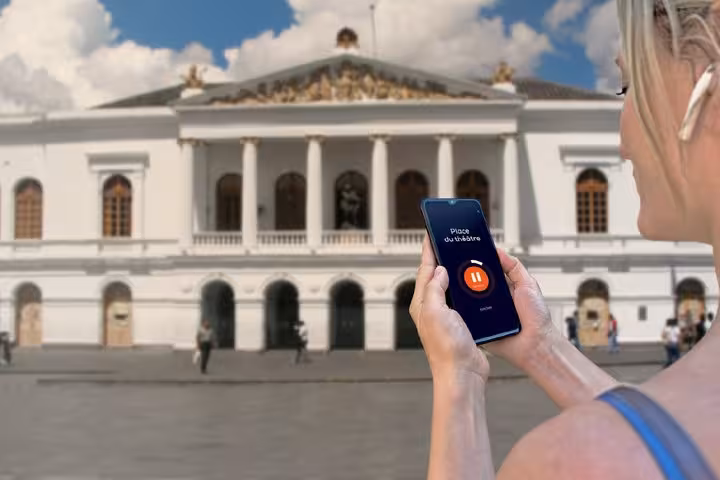 Woman using self-guided audio tour app on smartphone in front of Quito's historic theater building