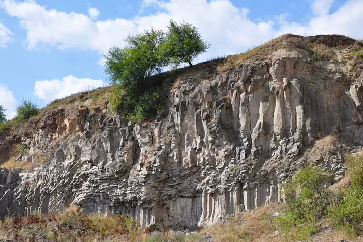 Rocky basalt columns cliff face at Racos quarry with green trees on top against blue sky