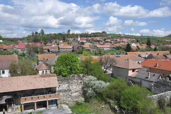 Aerial view of Racos village with terracotta rooftops, stone ruins, and green trees in Transylvania, Romania