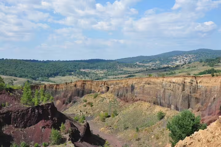 Colorful volcanic crater landscape at Racos with layered red and yellow rock formations surrounded by green hills