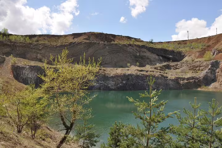 Turquoise lake in Racos volcanic crater quarry with layered rock walls and green trees, Brasov region