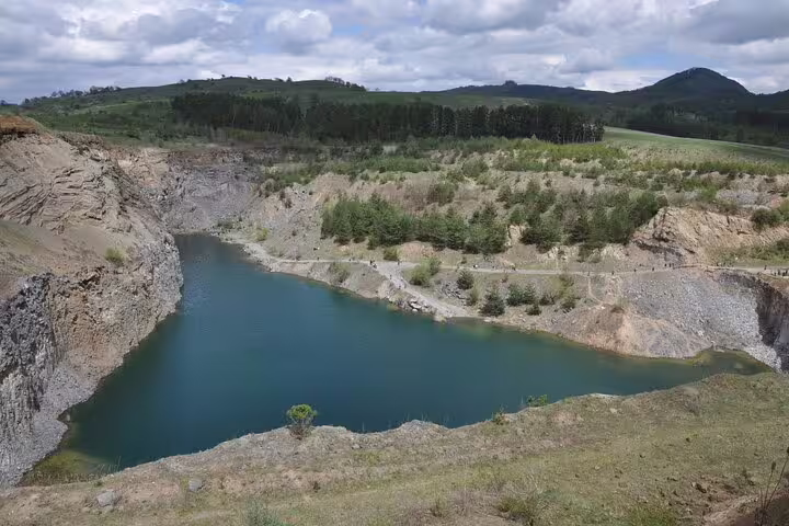 Turquoise volcanic lake in Racos basalt quarry surrounded by rocky cliffs and pine trees, Transylvania