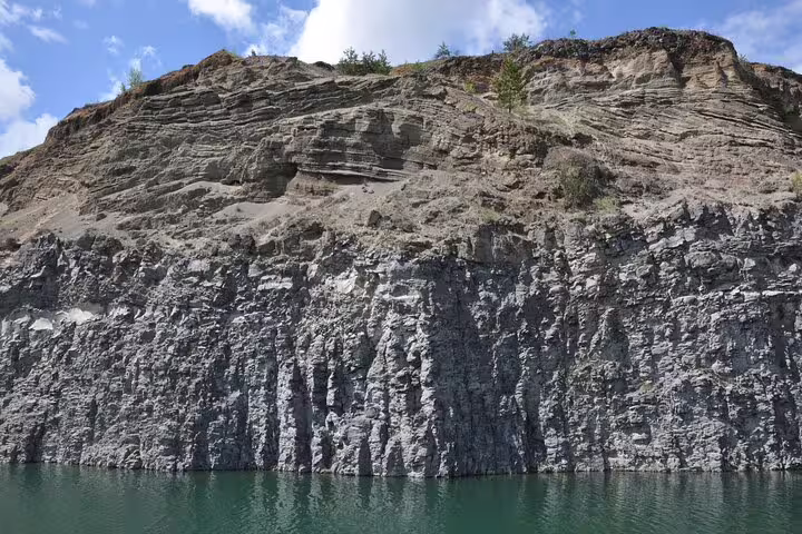 Dramatic rocky cliff face with layered sediment above turquoise water at Racos volcanic lake, Romania
