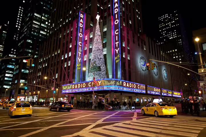 Radio City Music Hall at night with neon lights and yellow taxis on Midtown NYC street