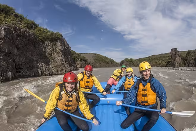 Smiling rafting group paddling an inflatable raft through canyon rapids on the 04C Riding and Rafting tour