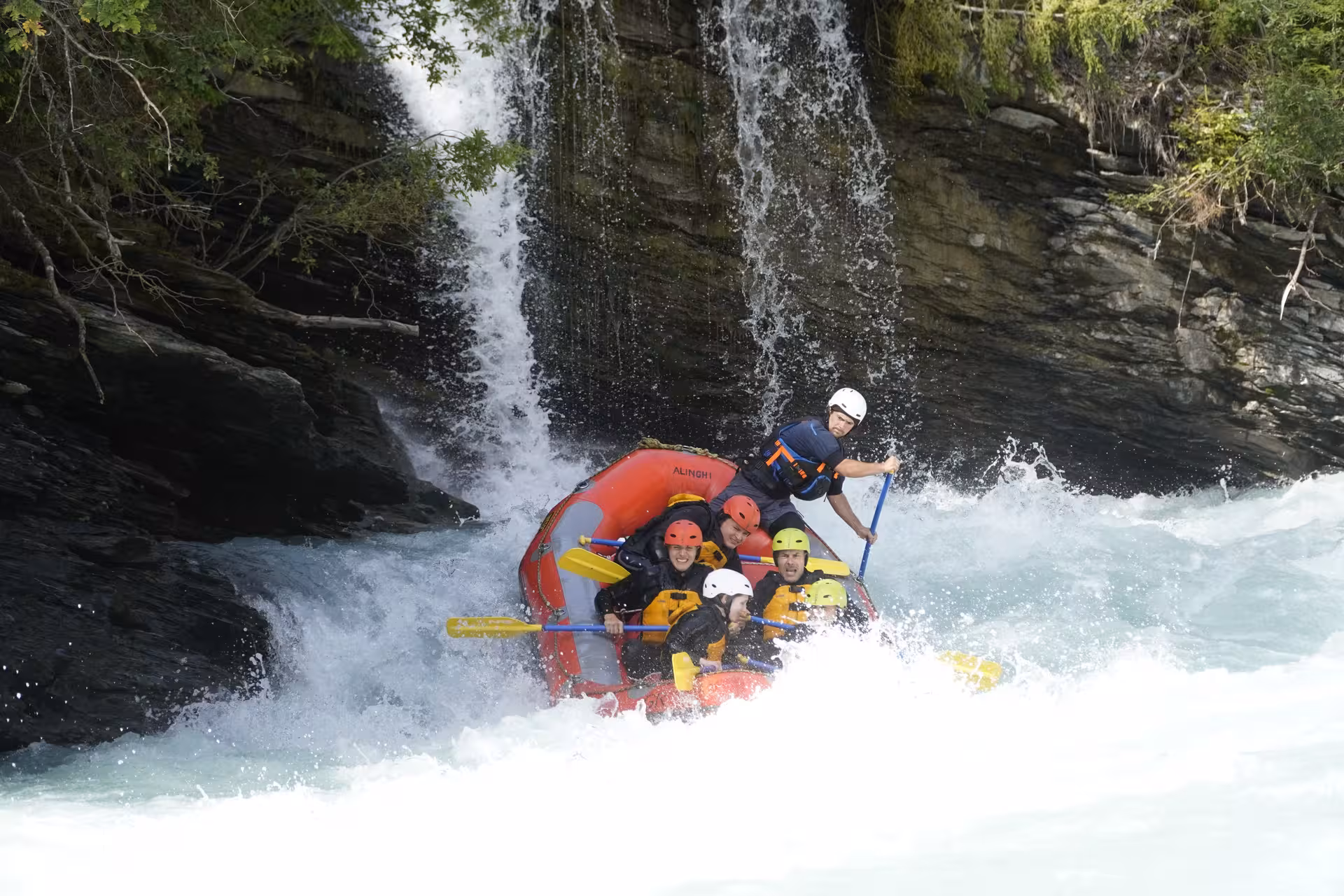 Adventurers rafting under a waterfall in Interlaken, highlighting the exhilarating and scenic whitewater experience.