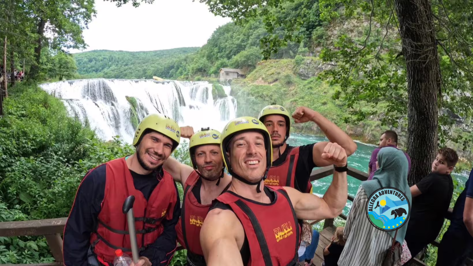 Rafting group in helmets and life vests posing by Una River waterfall, guided rafting tour from Plitvice Lakes National Park