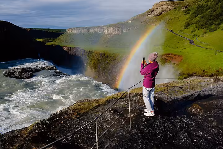 Tourist photographing a rainbow over Gullfoss waterfall on Iceland's Golden Circle tour