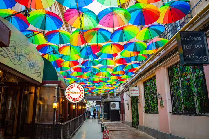 Colorful rainbow umbrellas hanging over a narrow alley in Bucharest Old Town with restaurants on both sides