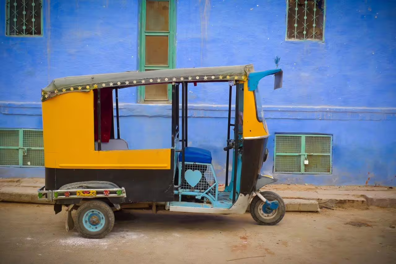 Colorful auto rickshaw parked against vibrant blue wall in Rajasthan, showcasing local culture on a 9-day tour.