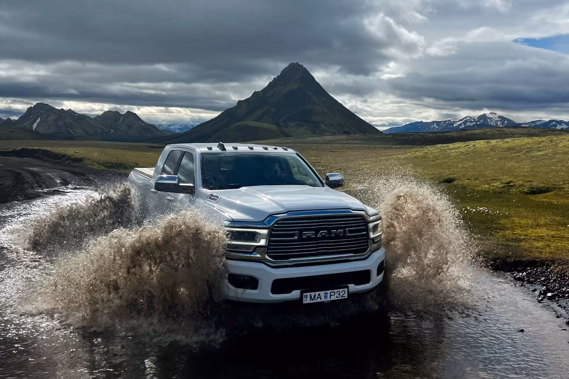 White RAM pickup super jeep splashing through river crossing in Fjallabak Nature Reserve with dramatic mountain backdrop