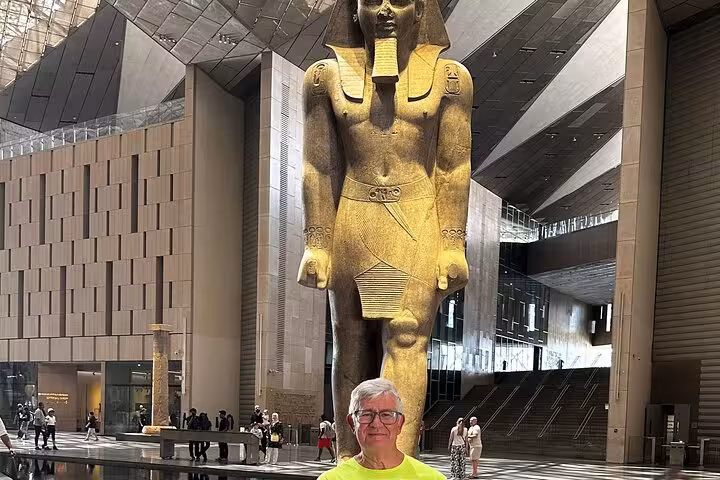 Tour guest posing by the towering Ramses II statue in the Grand Egyptian Museum during a Cairo day tour