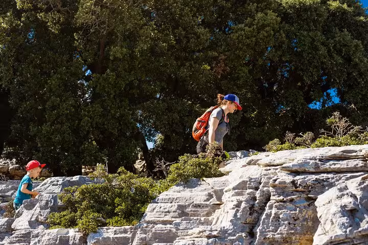 Family hiking rocky Randi’s Forest trail on Ikaria island, exploring cliffs and pine trees before Seychelles Beach boat trip