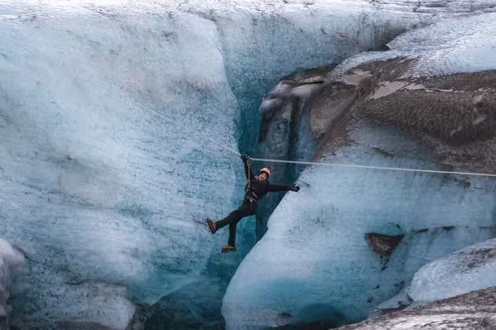 Smiling climber rappels between towering blue ice walls on a thrilling glacier adventure tour at Glacier Lagoon