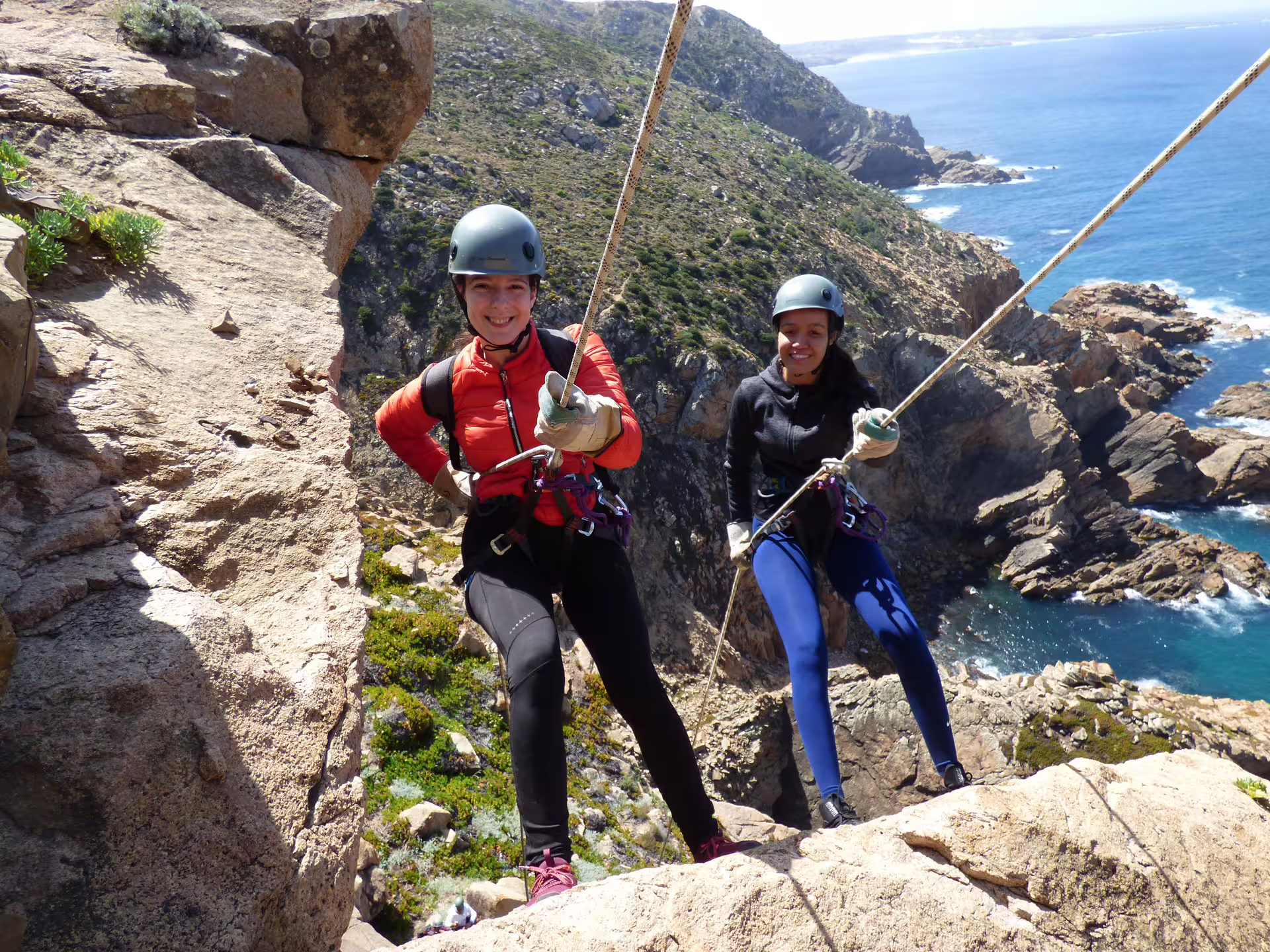 Adventurers rappelling down a rocky cliff with stunning ocean views in Sintra, Portugal, showcasing exciting outdoor activities.