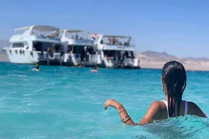Swimmer in turquoise Red Sea near tour boat on Ras Mohammed and White Island snorkeling excursion, Sharm