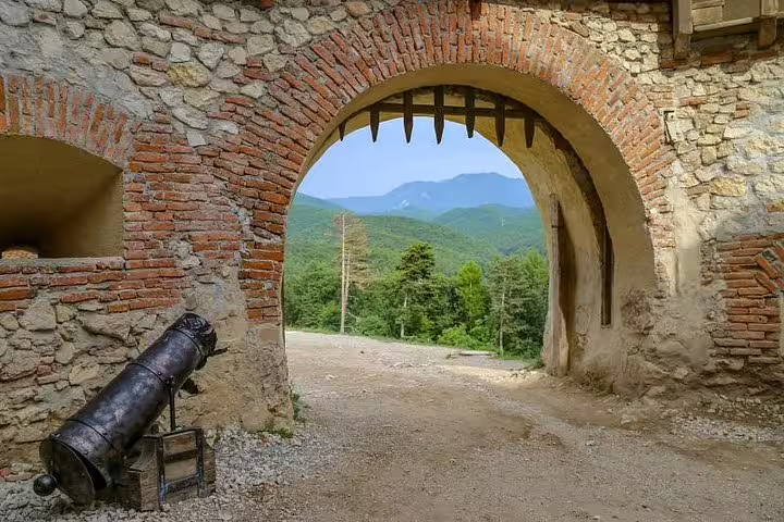 Ancient stone gateway with cannon at Rasnov Fortress, framing forested Carpathian mountains beyond
