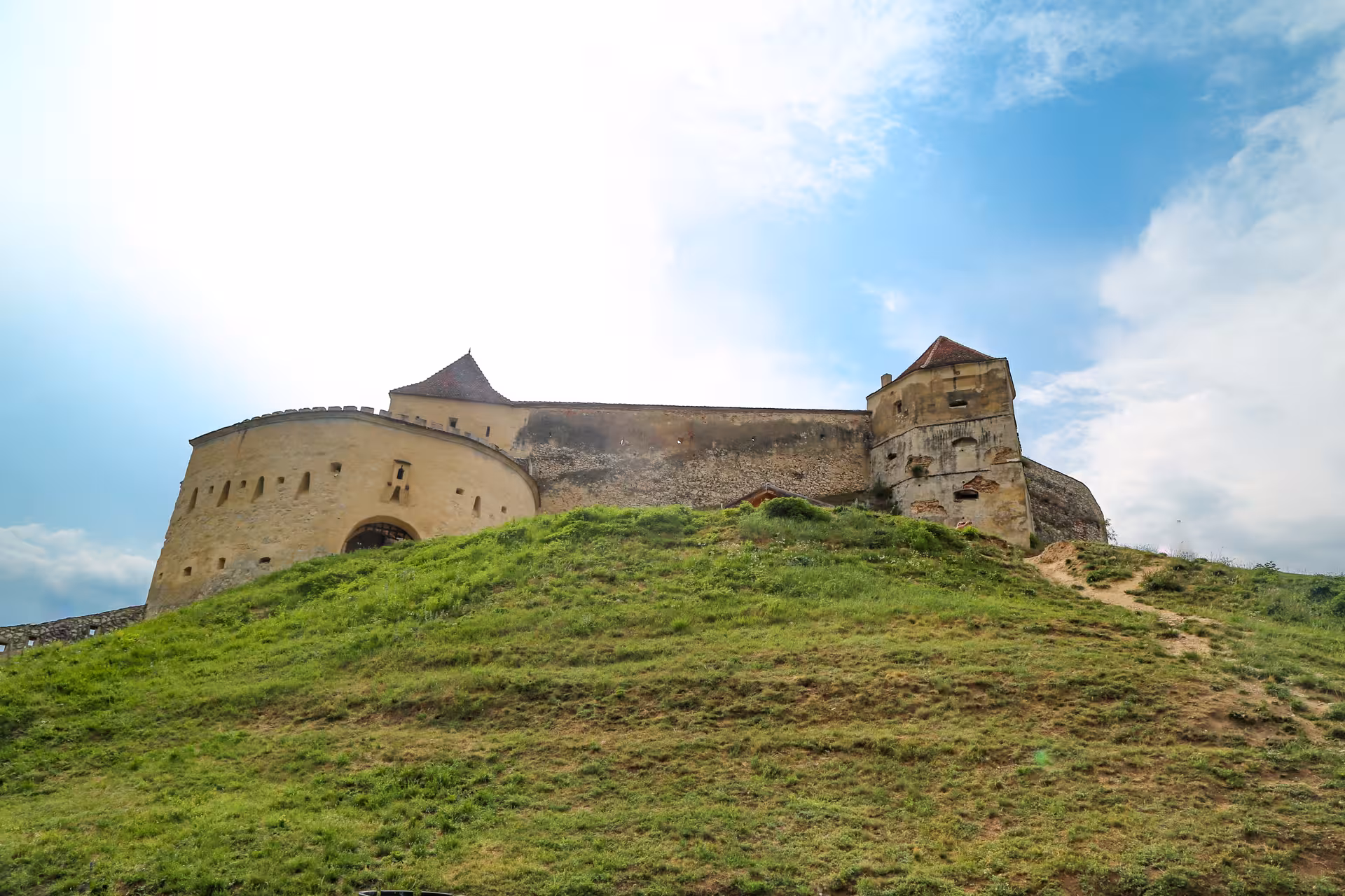 Rasnov Fortress medieval stone walls and towers on a green hilltop under blue sky, Transylvania Romania
