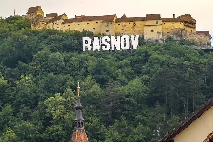 Rasnov Fortress on a forested hilltop with large white letters spelling RASNOV, Brasov Romania