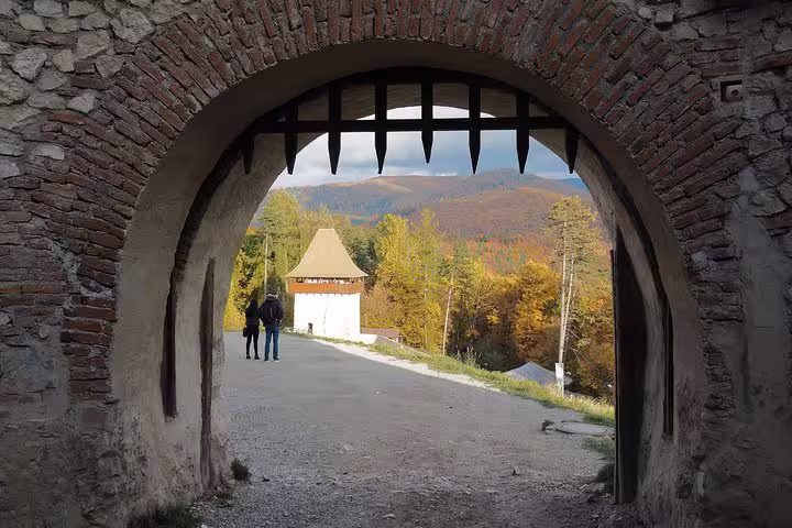 Medieval stone archway with portcullis at Rasnov Fortress, two visitors and autumn hillside beyond