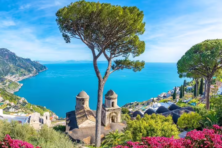 Panoramic view of Ravello's church domes, lush gardens, and turquoise Amalfi Coast from Villa Rufolo terrace