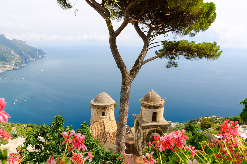 Enchanting view of Ravello's iconic domes and Mediterranean Sea, surrounded by flowers, on an Amalfi Coast day trip.