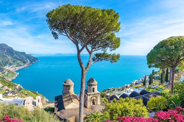 Panoramic view of Ravello's church domes, lush gardens, and turquoise Amalfi Coast from Villa Rufolo