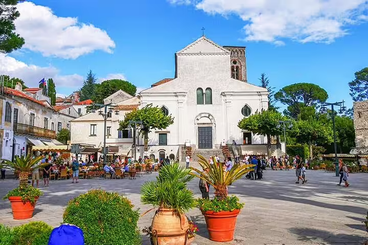 Piazza del Duomo in Ravello with white cathedral, outdoor cafes, and tropical plants on sunny day