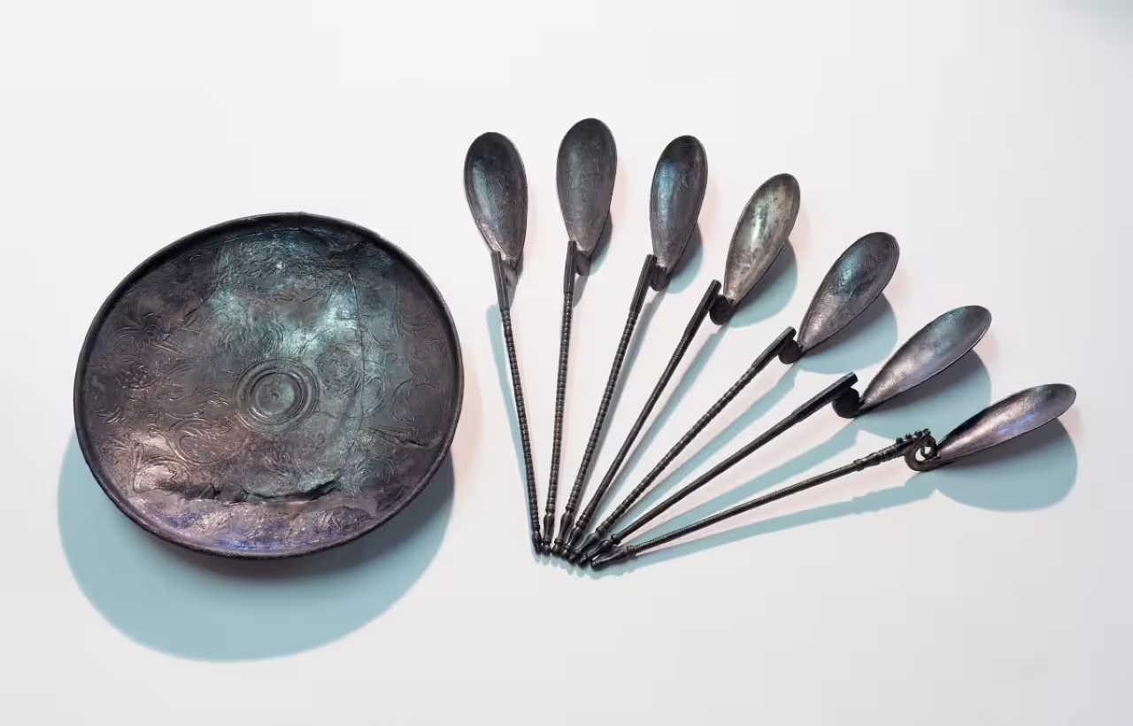 Roman-era metal spoons and engraved dish on display at Ravenna Classis Museum with entry ticket