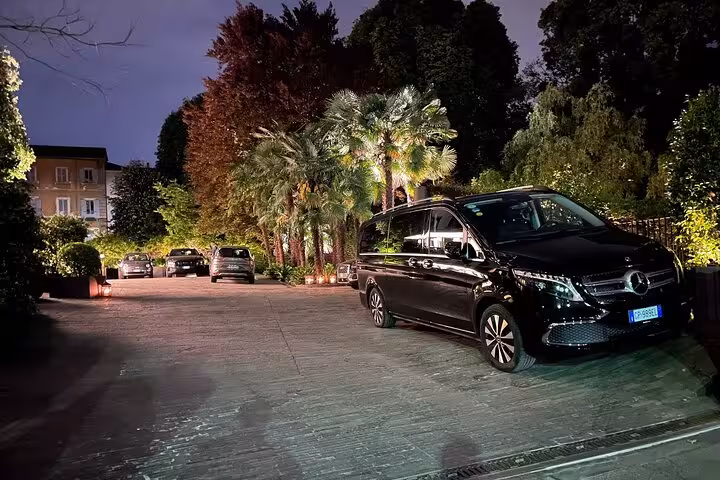 Elegant black van parked at night surrounded by lush greenery, offering premium transfer service to Bologna Airport.
