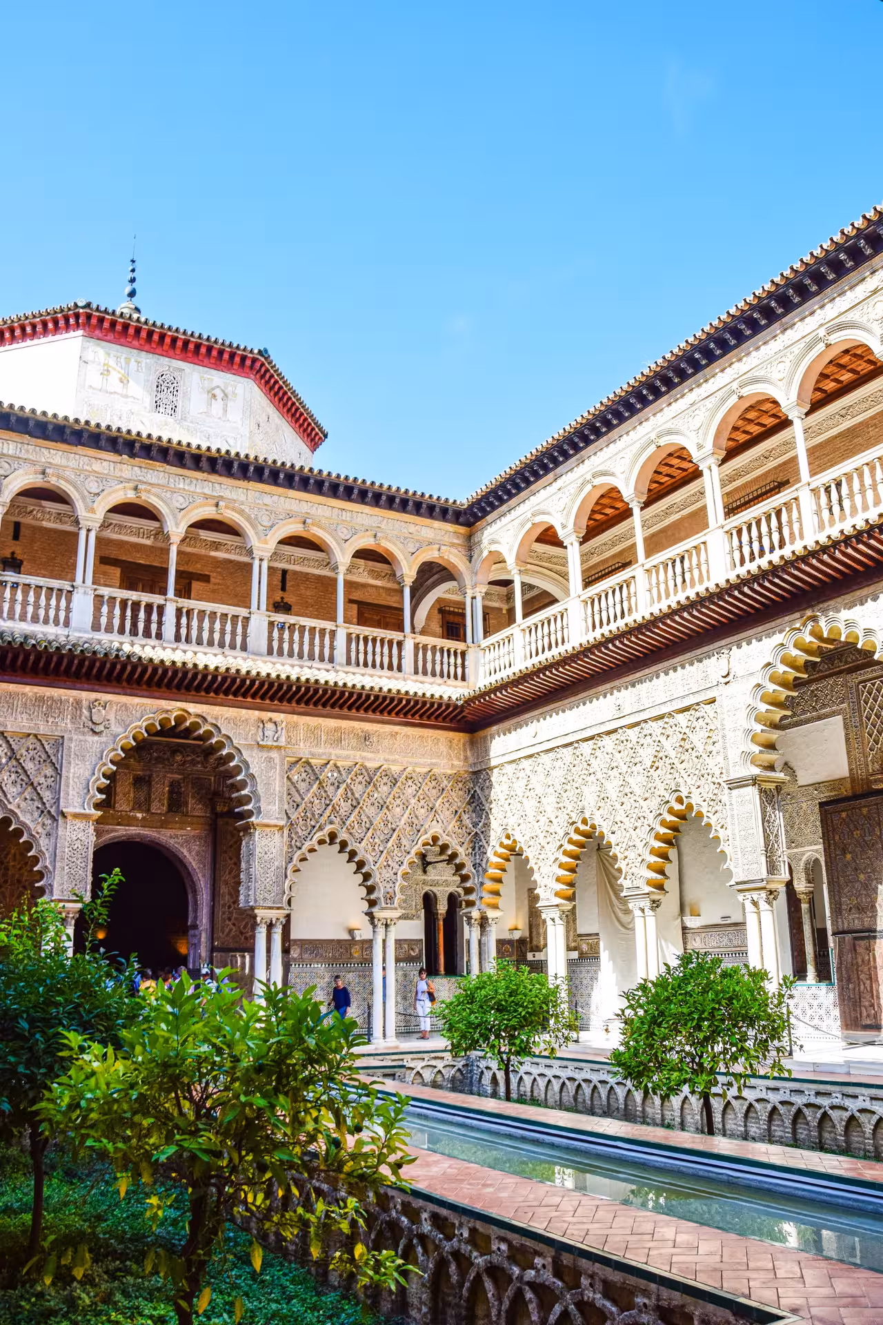 Sunlit courtyard of the Real Alcázar of Seville featuring lush greenery and exquisite Mudejar archways.
