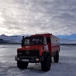 Red Mercedes 4x4 expedition truck on frozen glacier landscape in Iceland with snow-capped mountains