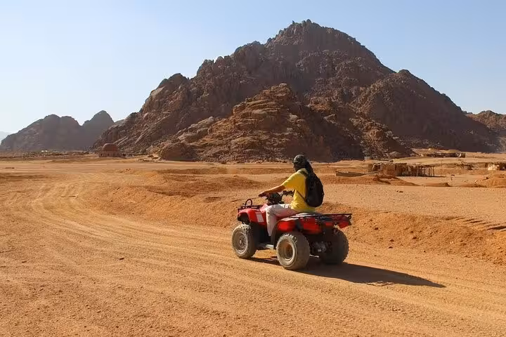 Single rider on red ATV quad bike in Hurghada desert safari trail with rocky mountains, before camel ride stop