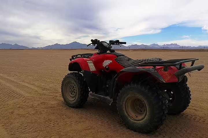Red ATV quad bike parked in Marsa Alam desert, Egypt, ready for quad safari and camel ride adventure tour