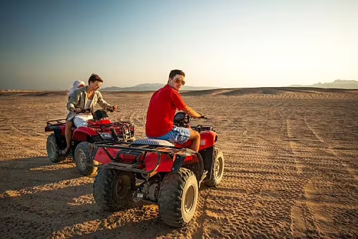 Riders on red ATVs crossing Sinai desert at sunset on a private quad bike safari from Sharm El Sheikh