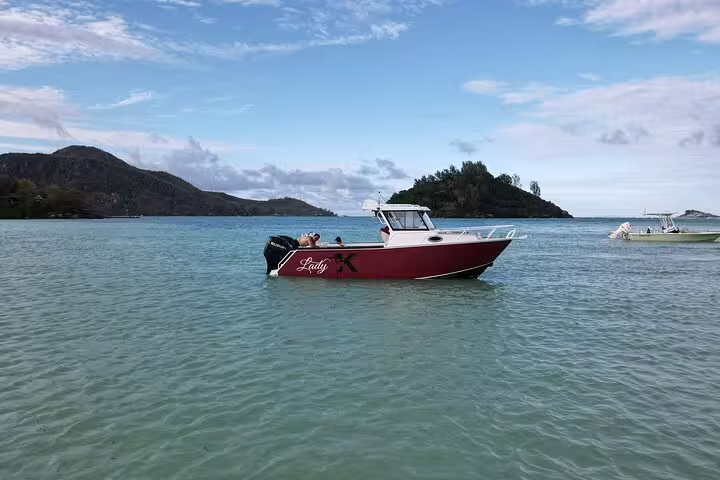 Red boat 'Lady X' anchored in the clear waters of Seychelles with scenic island views, perfect for fishing adventures.
