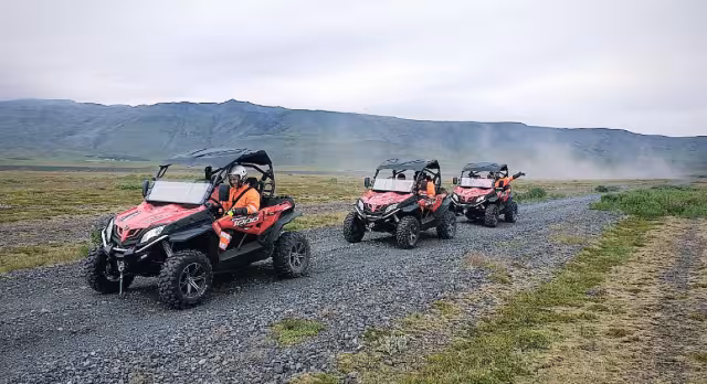Three red off-road buggies driving in a line on a gravel trail with misty Icelandic mountains behind