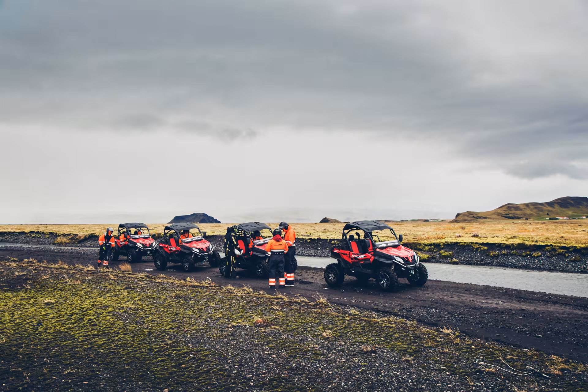 Group of red off-road buggies parked on volcanic terrain in Iceland with riders in orange safety gear